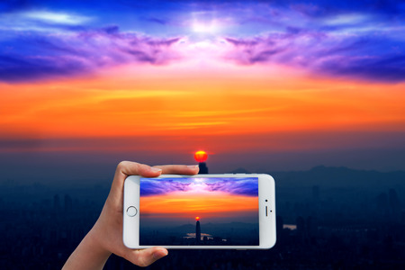Hand holding smart phone take a photo at Sunset and beautiful sky at Lotte world mall in Seoul.の写真素材