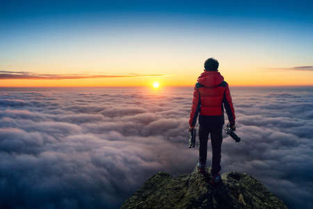 Photographer hand holding camera and standing on viewpoint over clouds. Panorama viewpoint at sunrise.の写真素材