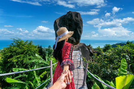 Women tourists holding man's hand and leading him to overlap stone at Koh Samui, Thailand.の写真素材