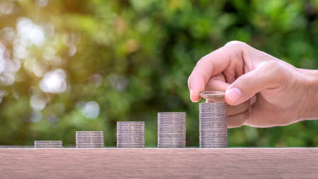 Hand holding coin and stack of money on wood table. Pension fund concept.