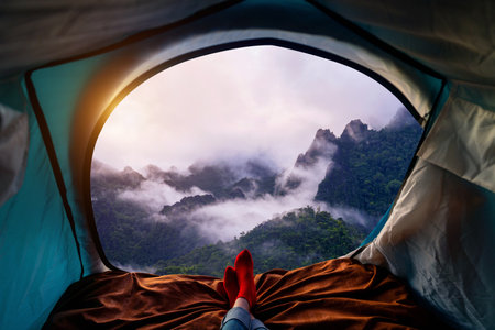 Woman cross leg on blanket in camping tent with sleeping bags on mountain hill. view from inside with limestone mountains covered by mist in Vang vieng, Laos.の写真素材
