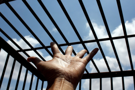 Hand of the prisoner on a steel lattice close up (jail, prison, man)の写真素材