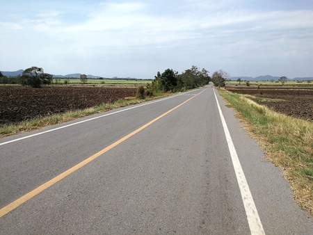 wide open prairie with a paved highway stretching out as far as the eye can see with beautiful under a bright blue sky in the summer time.の写真素材