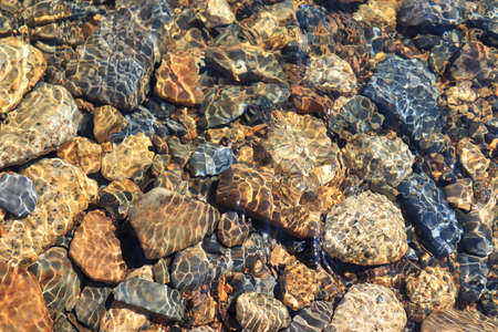 Abstract background: the orange and gray stones in pure transparent mountain river water, Magadan...