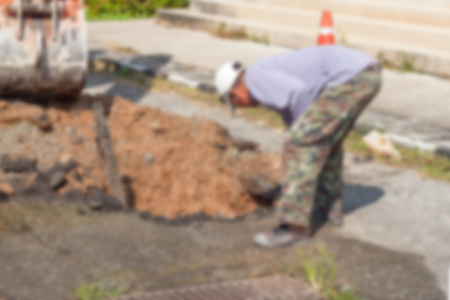 Blur blurred Plumbing Repair Man and excavator scoop digging,  Worker using a small tracked excavator to dig a hole to fix a water on the road, and soft-focus background.の写真素材