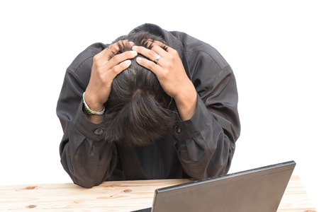 Worried businessman . a young man sits at his Desk and holds his hands on his head, on white background.の写真素材