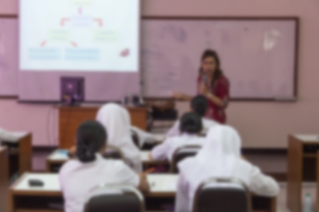 Blurred abstract background of university students sitting in a lecture room with teacher in front of the class with white projector slide screen: Blurry view from back of the classroom: Teachers dayの写真素材