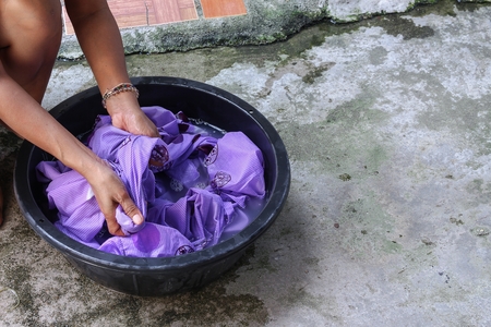 Woman wash hands dirty clothes in the basin black for cleansing,Thailand washing clothes style ancient and soak with detergent in the evening.の写真素材