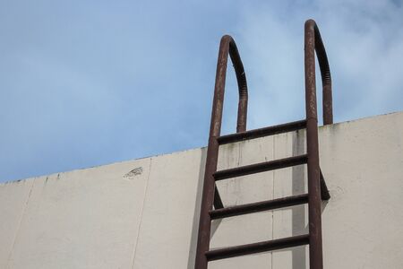 Old vertical industrial metal rusted ladder. Staircase to Water tank no safety rails. sky background with copy space.の写真素材