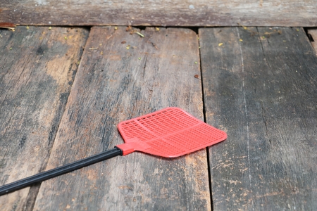 Red fly swatter. Single flyswatter made of plastic and unfailing in catching flies on Wooden floor backgroundの写真素材
