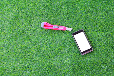smart phone and red cutter knife on artificial grass backgroundの写真素材