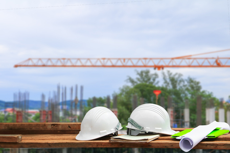 safety helmet plastic and blueprint on wood with blur construction building site workplace backgroundの写真素材