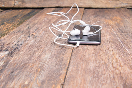 white earphone on mobile phone with table old wooden vintage background and copy space select focus with shallow depth of fieldの写真素材