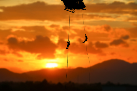 soldier silhouette in rappelling climb down from helicopter on sunset