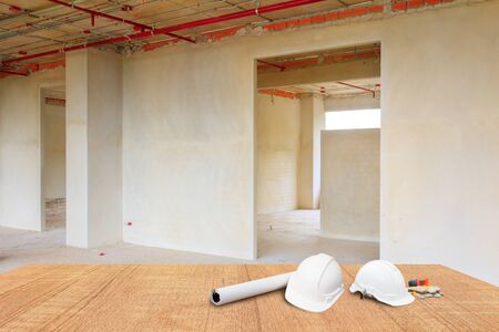two white safety helmet and leather glove Measuring Tape, roll paper plan blueprint for engineering working interior construction site building on wood floor table with copy space add text. blur backgroundの写真素材
