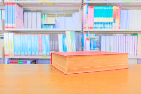old book red in school library on wooden table. blurry bookshelves background. education learning concept with copy space add textの写真素材