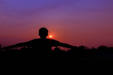 Silhouette of male meditating and yoga practicing with exercise at sunrise in public park morning