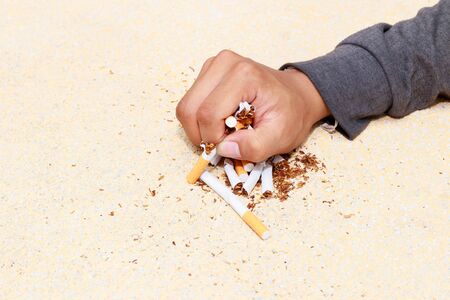 male hand crushed pile cigarettes Close up on table terrazzo flooring yellow background. health care concept stop quitting smoking.の写真素材