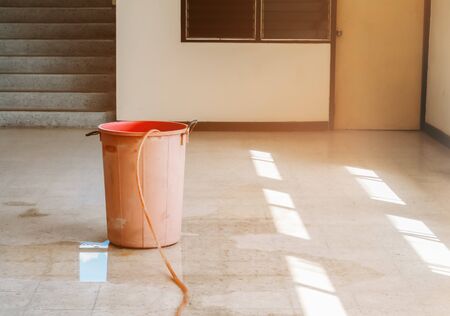 water leak drop interior office building in red bucket from Ceiling and flow on terrazzo floorの写真素材