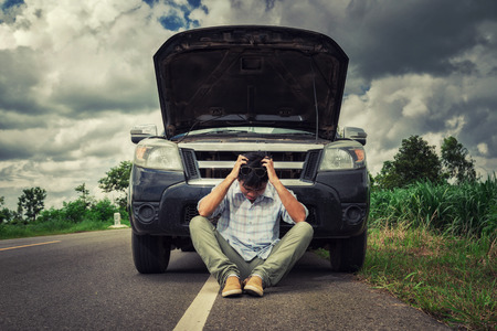 young stressed man having trouble with his broken car looking in frustration on failed engineの写真素材