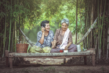 Two Asian old women sat happily on the bed in a Thai bed. Communication concept with descendants over the phone.の写真素材