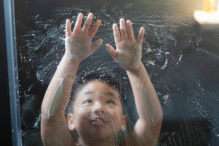 A boy plays with soap bubbles on the glass in the shower.の写真素材