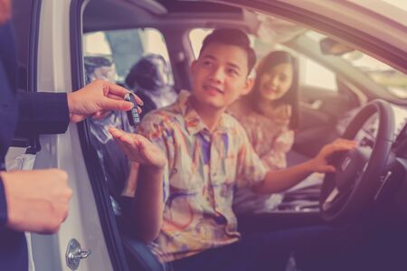 Car sales giving the key of the new car to the young attractive owners. Couple purchasing brand new...
