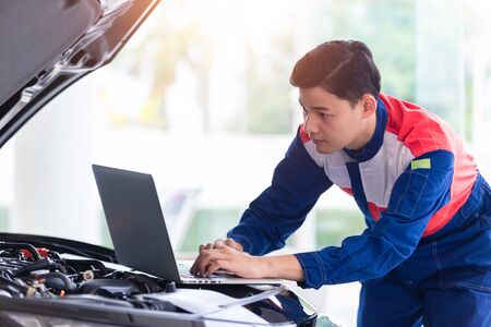 Professional mechanic in uniform is Check the quality of new car engine oil before delivering to customers. while working in car repair center by using a laptop as a work tool.の写真素材