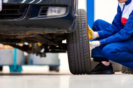mechanic in uniform is changing a wheels/tires while working in car repair centerの写真素材