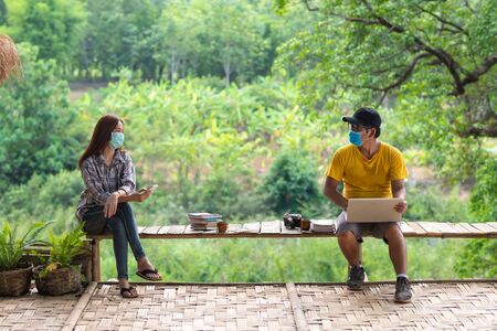 Asian woman and man in social distancing sitting on bench in the middle of nature, Social distancing concept.の写真素材