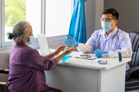 Asian doctor advised the old woman to wash her hands with alcohol before the treatment to prevent the initial corona virus infection.の写真素材