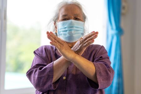 Senior asian woman wearing face mask during corona virus and flu outbreak. Disease and illness protection. show stop hands gesture for stop corona virus outbreak.の写真素材
