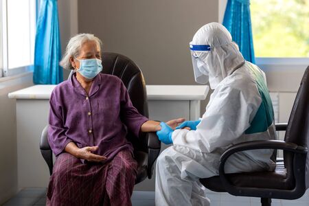 Asian doctor is checking patience's pulse by fingers, medical checking on table. the aging female patient that is at risk for infection corona virus [covid-19].の写真素材