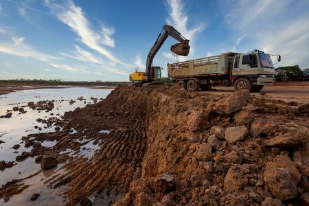 excavator at sandpit during earthmoving works ifilling a dump truck with rock and soil for fill at a new commercial development road construction projectの写真素材