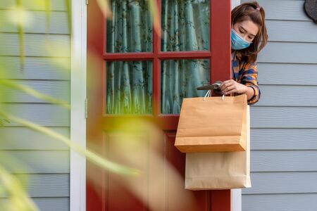 Asian woman wearing a mask Received the item delivered to the front door of the house concept service quarantine pandemic coronavirus virus [Covid-19]. Stay at home, New normalの写真素材