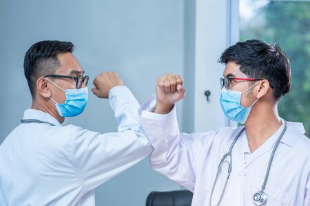 Elbow bump. New novel greeting to avoid the spread of coronavirus. Two doctor friends meet in The hospital with bare hands. they bump elbows instead. New normalの写真素材