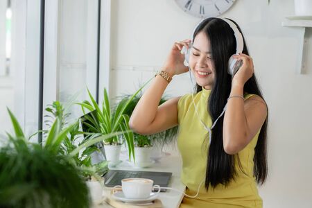 Asian smiling girl student wear wireless headphone study online with skype teacher in a coffee shop, woman learn language listen lecture watch at laptop sit in cafe, distant education, New normalの写真素材