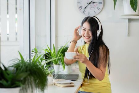 Asian smiling girl student wear wireless headphone study online with skype teacher in a coffee shop, woman learn language listen lecture watch at laptop sit in cafe, distant education, New normalの写真素材