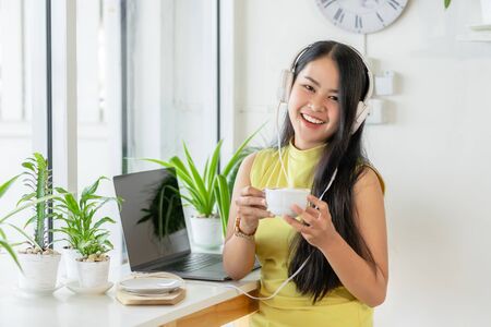 Asian smiling girl student wear wireless headphone study online with skype teacher in a coffee shop, woman learn language listen lecture look at the camera sit in cafe, distant education, New normalの写真素材