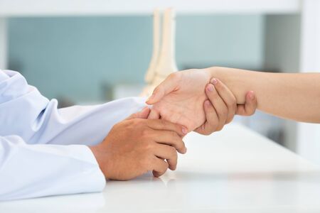 Asian doctor examining patient with wrist bone problems painful wrist caused by prolonged work on the laptop. Carpal tunnel syndrome, arthritis, neurological disease concept. Numbness of the handの写真素材