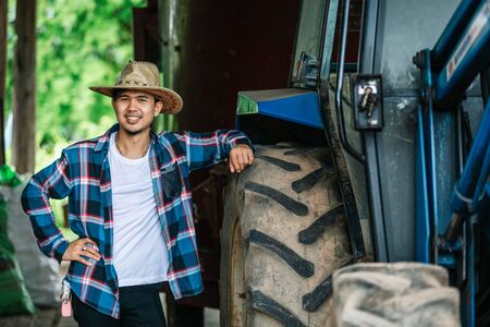 Portrait of a handsome asian young farmer standing in a shirt and smiling at the camera, on a tractor and nature background.の写真素材