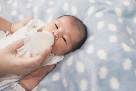Asian mom feeding bottle of milk to Newborn baby cute son in a bedroom.