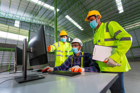 Asian Supervisor engineer Consult with warehouse workers, Inside the Heavy Industry Factory male Industrial Engineer Works on Personal Computer in the factory.の写真素材