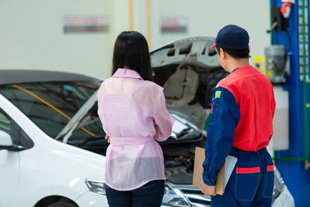Asian mechachic checking on a car engine and report the damage of the vehicle to the customer.の写真素材