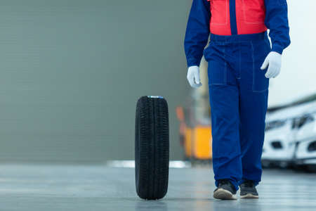 Auto mechanic change tire attractive auto mechanic man in blue uniform with blue gloves rolling wheel going on the autoservice in the auto repair centerの写真素材
