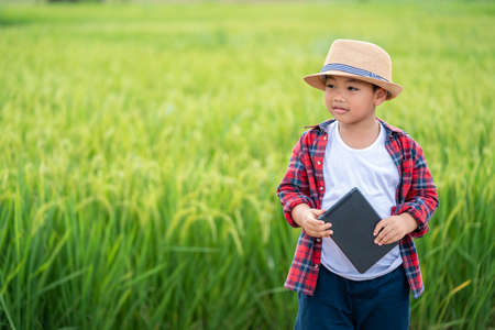 Happy Asian Little boy with a tablet interested in learning the surroundings in the green fields, education concept outside the classroom Educational freedom  In the age of technologyの写真素材