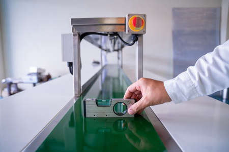 Close up of hand Mechanic technician worker use a water level meter working and Assemble the product sorting machine conveyer in industrial factory.の写真素材