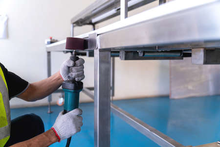 Close up of hand Worker use Electric wheel grinding on Polishing of varnish after painting the Aluminum on product sorting machine conveyer in industrial factory.の写真素材