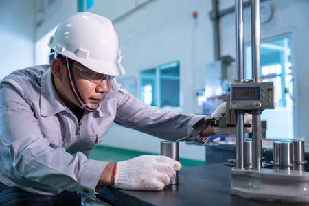 Asian technician worker wearing a safety suit and Quality Checking with hight gauge mass Product on Granite Surface Plate in industrial factory.の写真素材