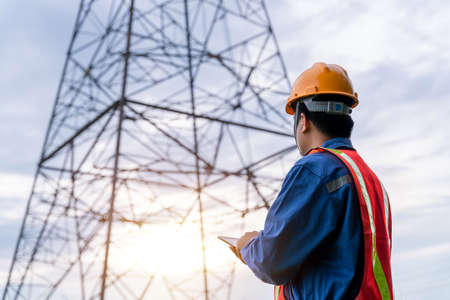 Electrical engineer wear safety clothes standing and watching at the electric power station to view the planning work by producing electricity at high voltage electricity poles.の写真素材